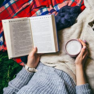 woman reads book holding cup coffee lying colorful plaids 1304 3359